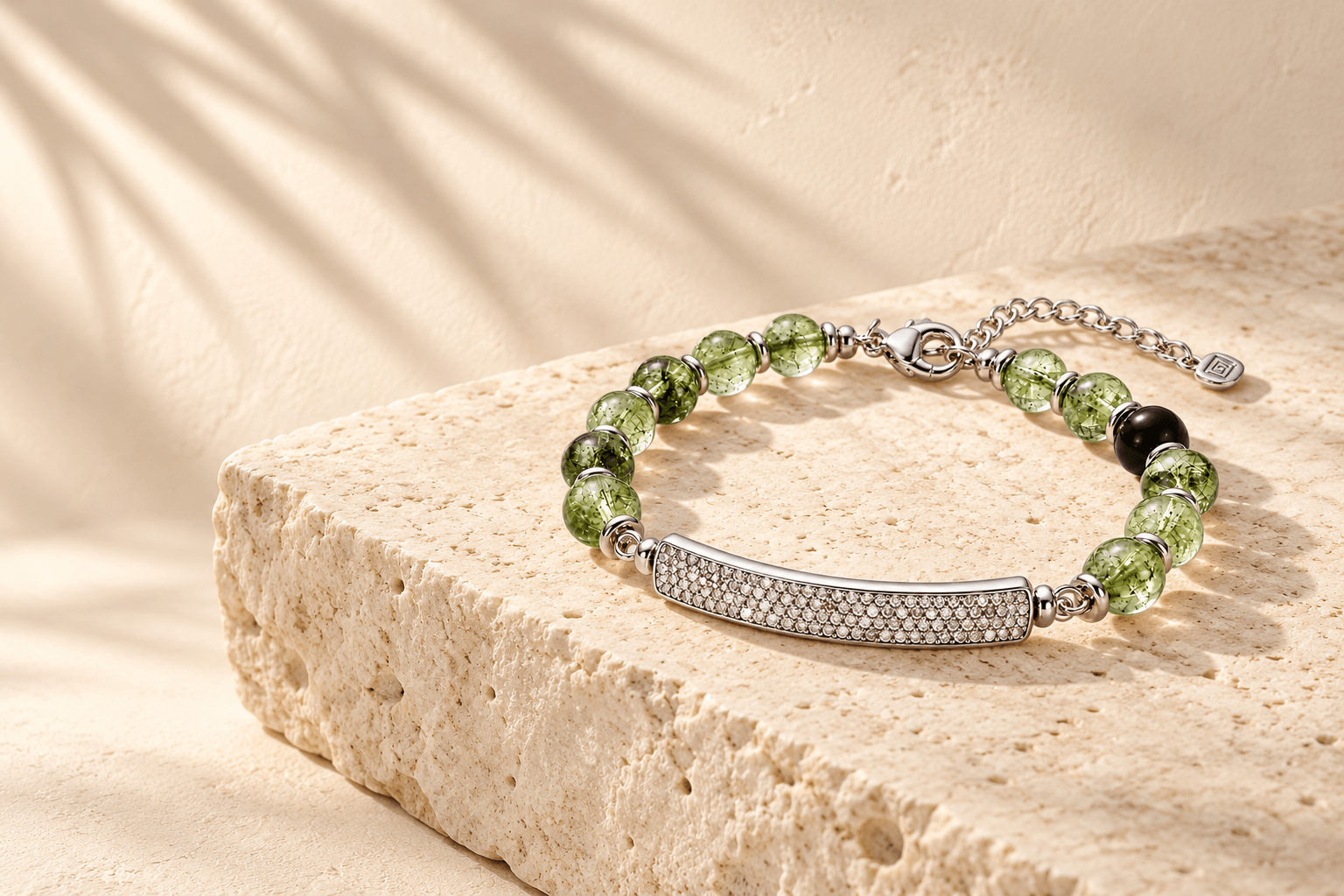 QiLyra bracelet of green quartz and a pavé diamond bar, resting on travertine with palm shadows.