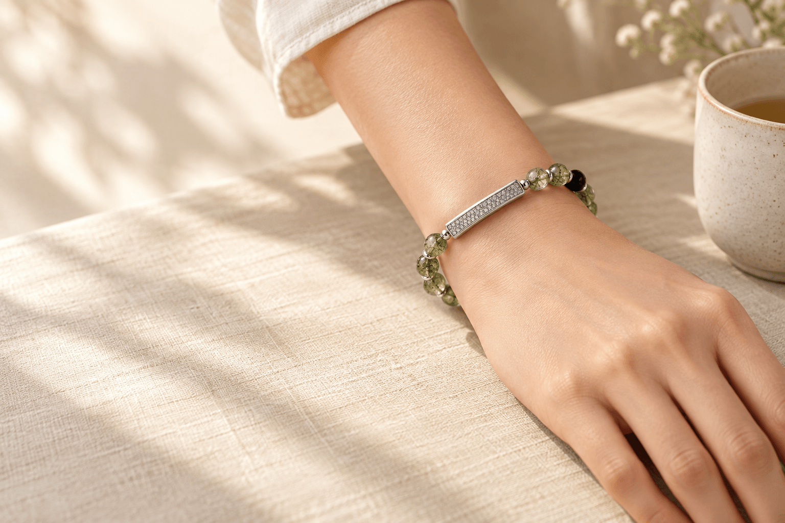 QiLyra bracelet on a wrist at a linen table, beside a cup of tea in soft window light.